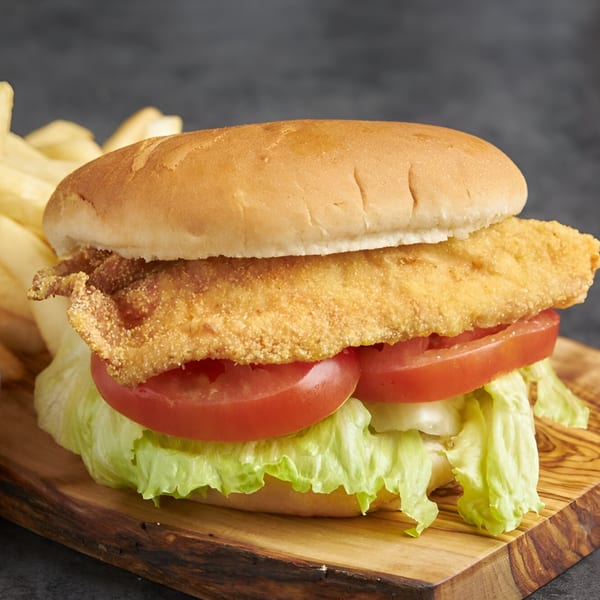 A Snappers fried fish sandwich with lettuce and tomato, served with fries on a wooden board.