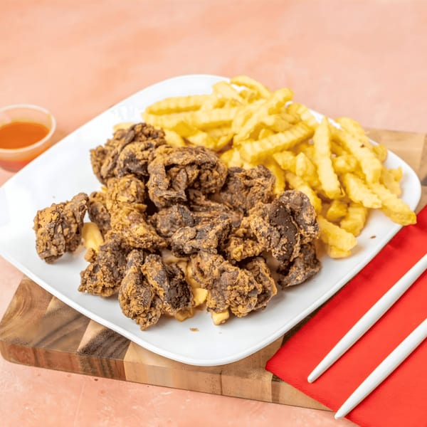 A white plate with fried gizzards and crinkle-cut fries, with a side of dipping sauce.