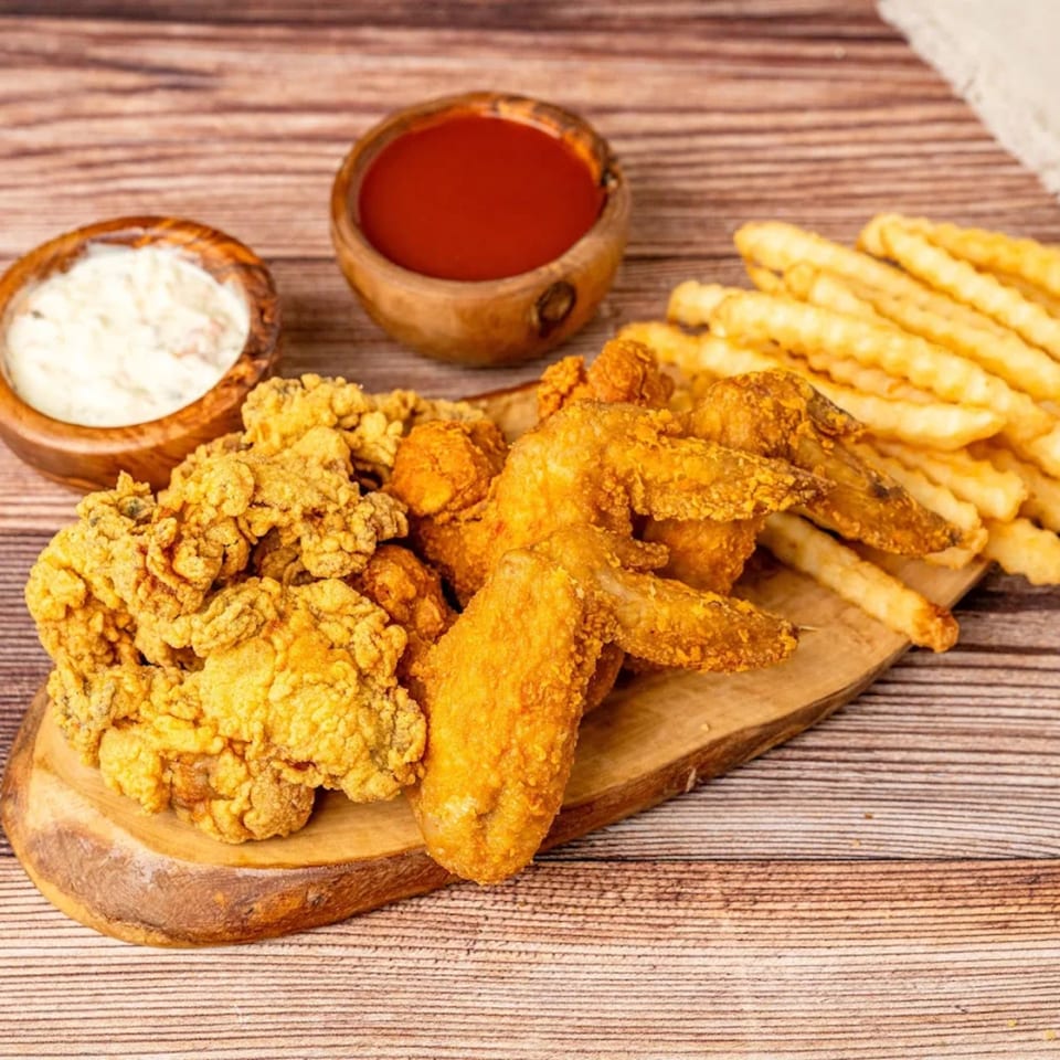 Crispy fried chicken pieces, wings, and crinkle-cut fries on a wooden board with dipping sauces.