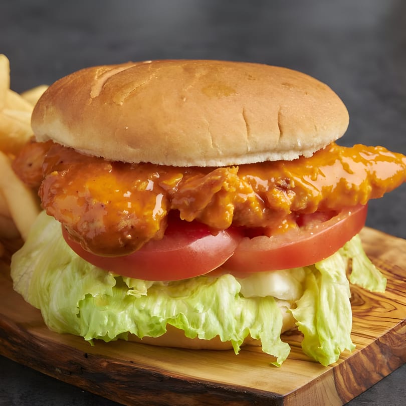 Snappers' buffalo chicken sandwich with lettuce, tomato, and fries on a wooden board.